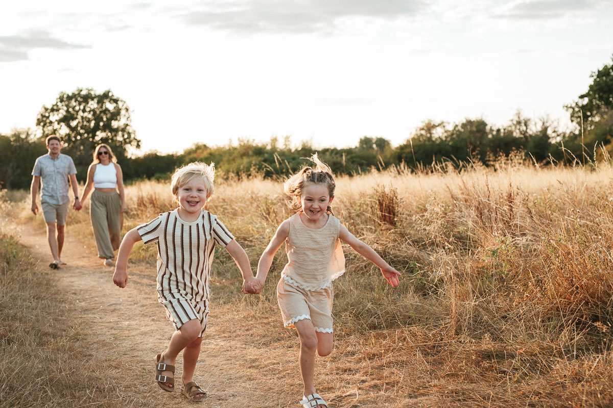 brother and sister running holding hands as their parents walk behind them during sunset in tadpole garden village