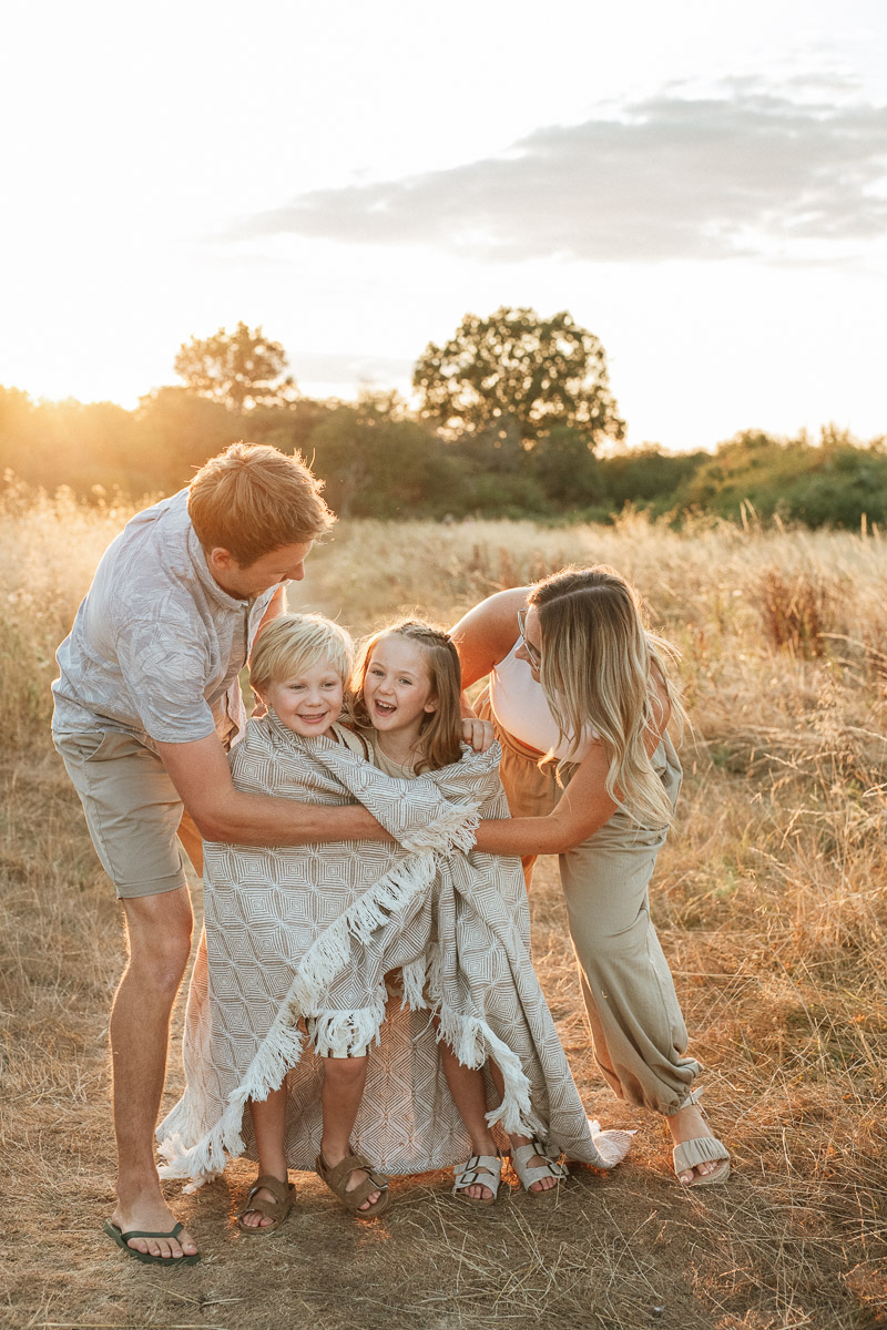 Family of four playing together during sunset at tadpole garden village. Mum and dad wrapping their children I n a blanket a they laugh