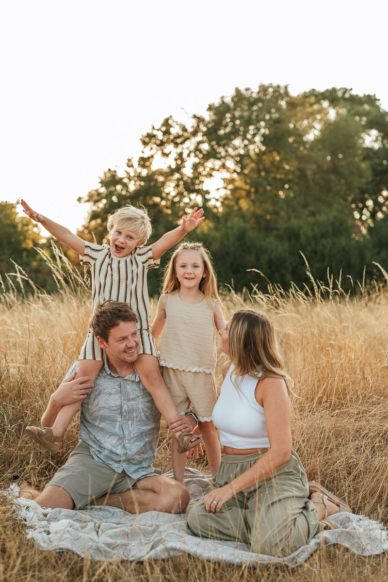 Parents and children playing together as they sit on a blanket during sunset. Captured by Wiltshire family photographer Rachel Jane