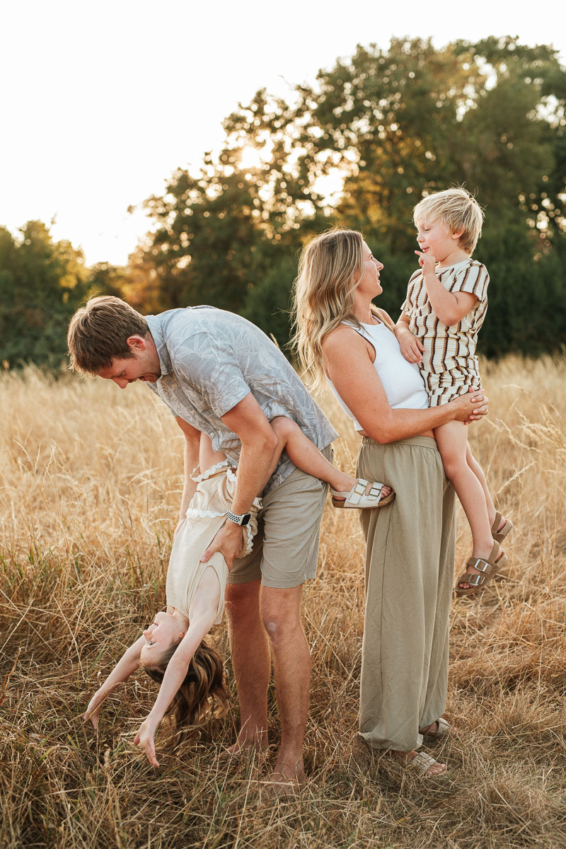 parents playing with their two children in a golden field during sunset. Captured by Wiltshire photographer Rachel Jane