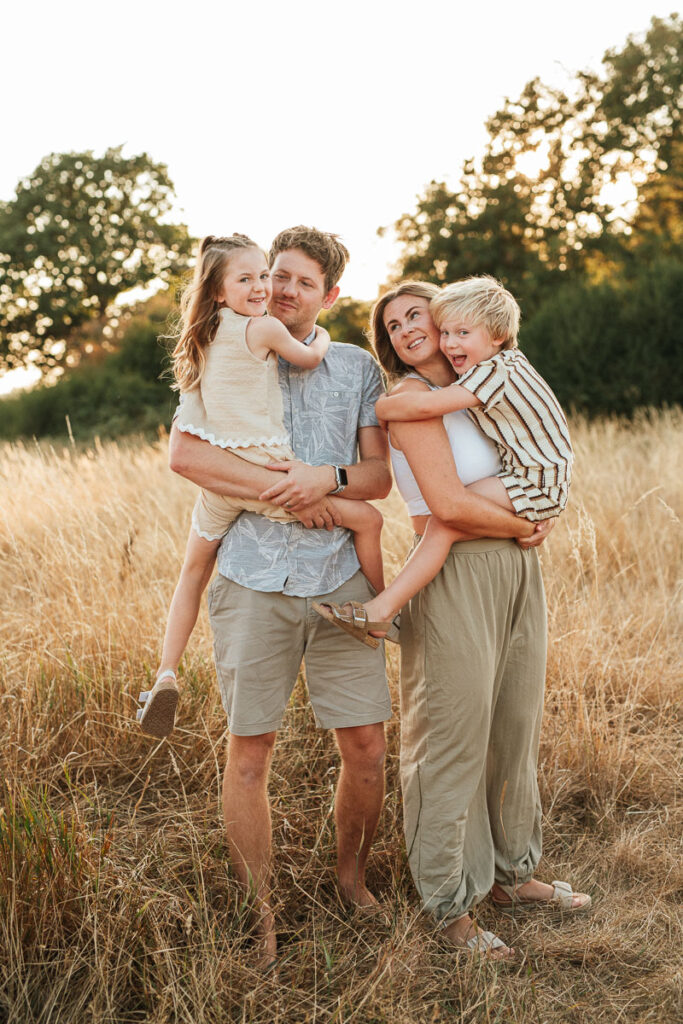 family of 4 standing in a golden field during sunset.