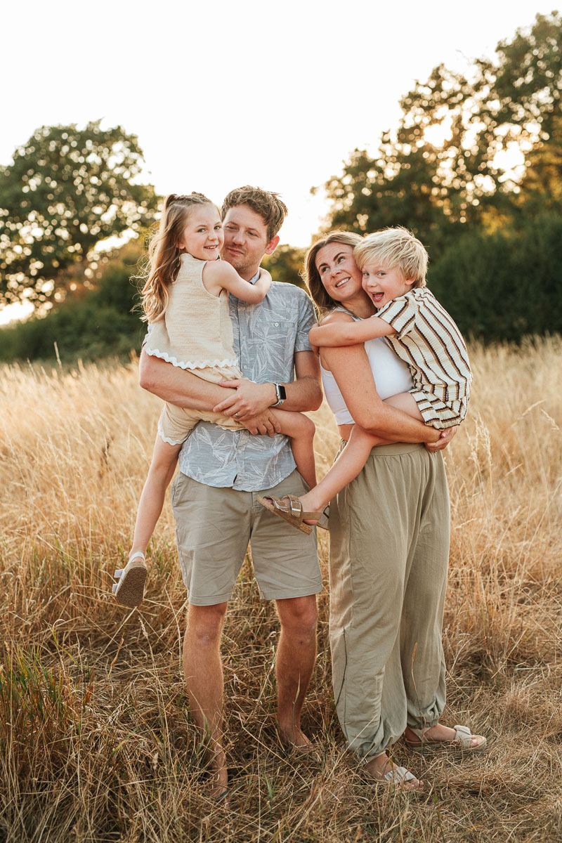 family of 4 standing in a golden field during sunset.