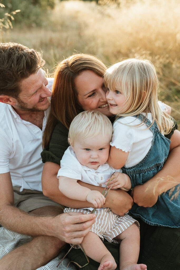 parents and children having a big hug as they sit on a blanket during sunset. Captured by Wiltshire family photographer Rachel Jane