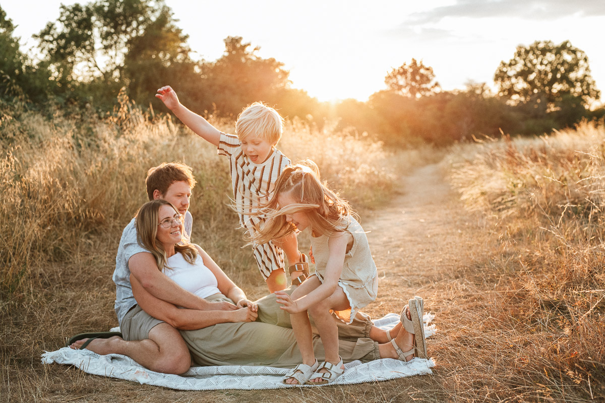 mum and dad sitting on a blanket as their two children run and jump over them during a relaxed family photoshoot