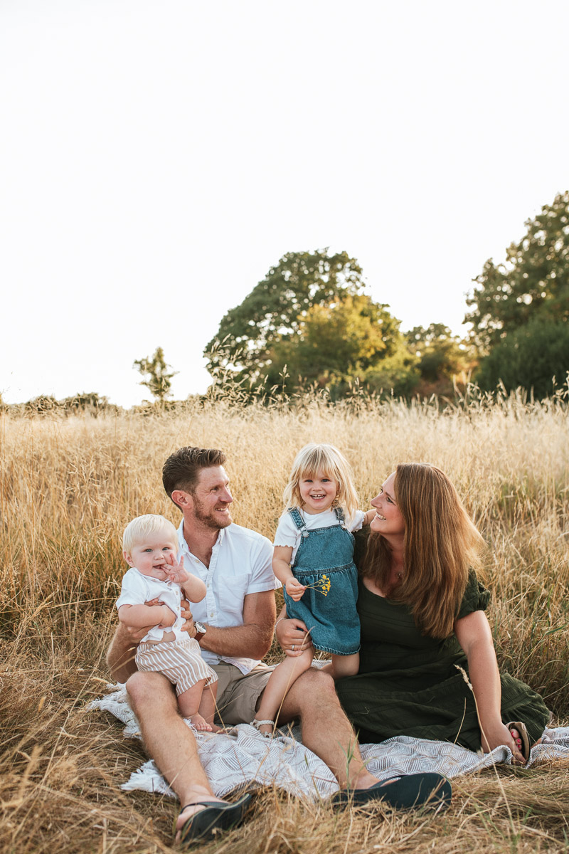 family of four sitting on a blanket in the long grass at tadpole garden village