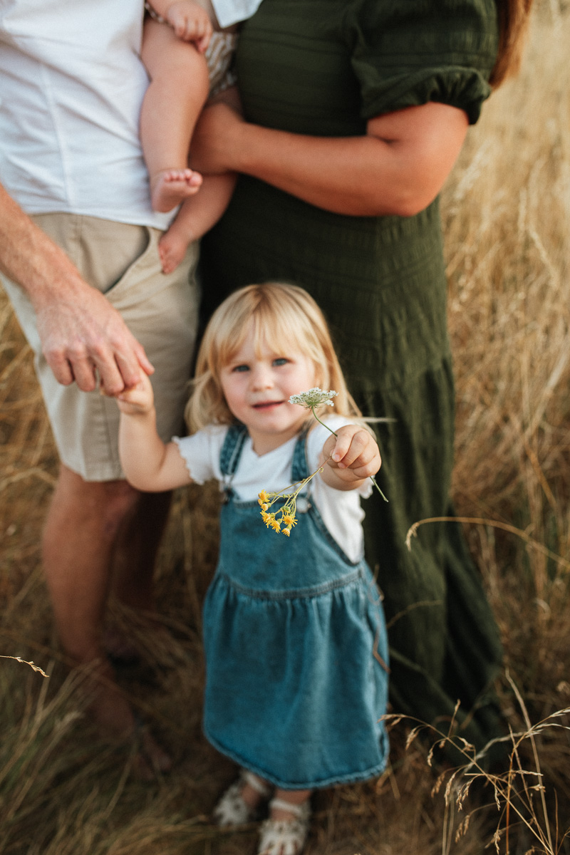 a little girl standing at her parents feet holding a yellow flower