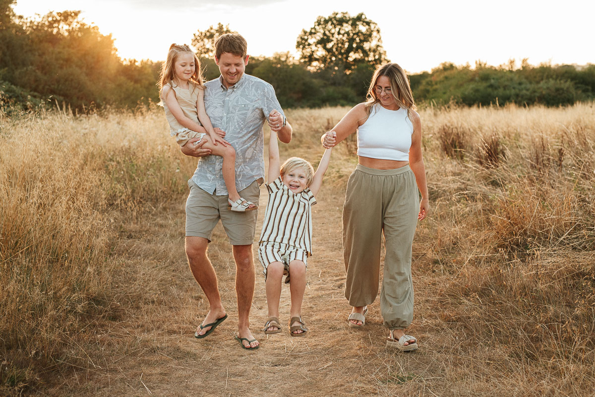 two parents swinging their little boy as they walk through the fields in tadpole garden village