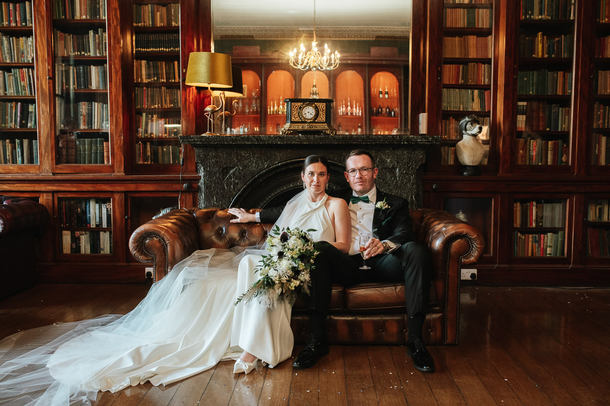 bride and groom sitting on a leather sofa posing for a formal portrait at grittleton house