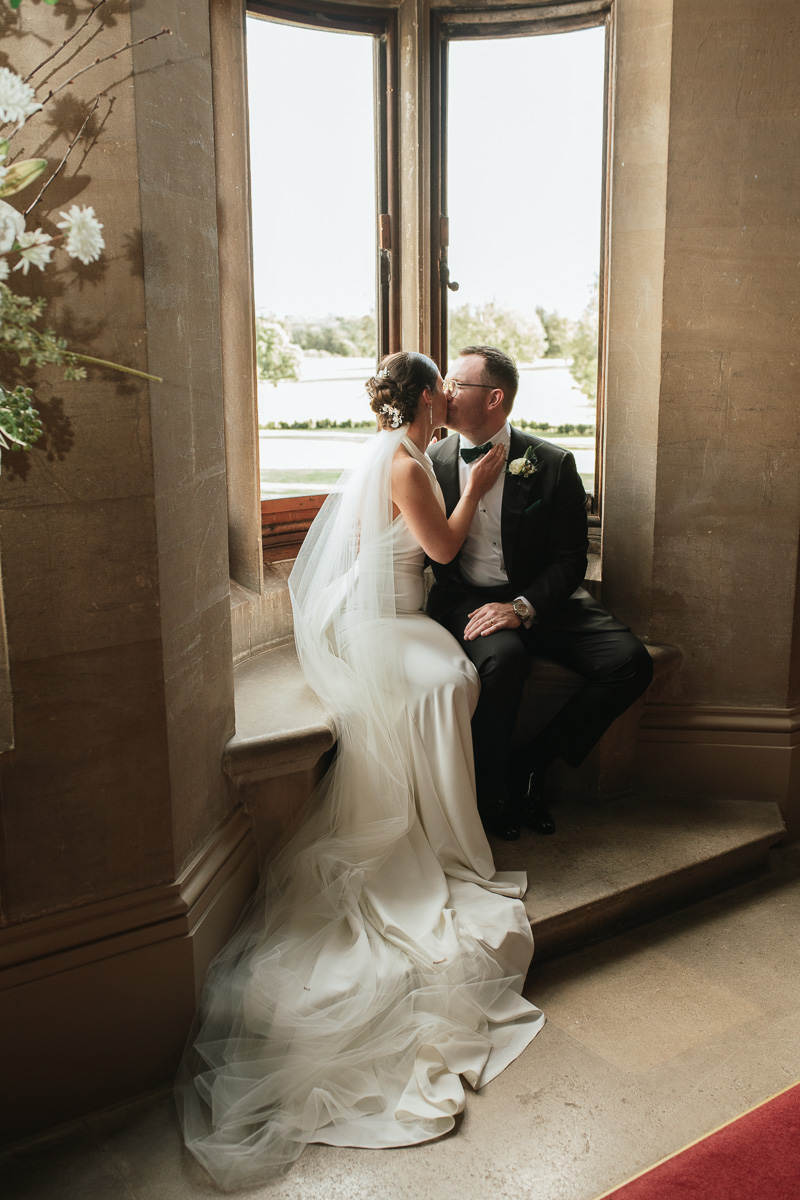 bride and groom sharing a kiss in the window by the stairs inside grittleton house